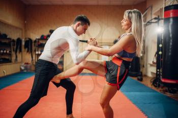 Female fighter hiding from a knife strike on self defense workout with male personal trainer, gym interior on background. Woman on training, self-defense practice