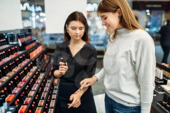 Seller consultant helps the woman with the choice of lipstick shade in the make-up shop. Cosmetic choosing in beauty store