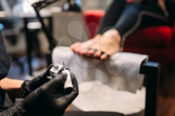 Pedicure master in black gloves paints with varnish foot nails of female client, beauty salon. Professional  fingernail care