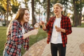 Love couple having fun with ice cream in summer park. Young man and woman leisures with ice-cream, romantic walk together outdoor