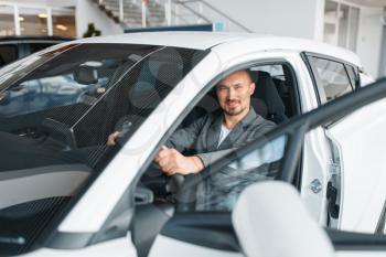 Man sitting in new car, showroom. Male customer choosing vehicle in dealership, automobile sale, auto purchase