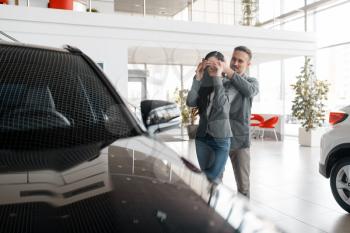 Couple buying new car in showroom, surprise for woman. Male and female customers choosing vehicle in dealership, automobile sale, auto purchase