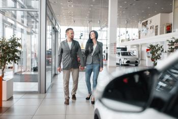Happy couple buying new car in showroom. Male and female customers choosing vehicle in dealership, automobile sale, auto purchase