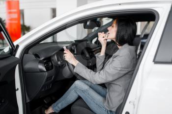 Woman buying new car in showroom, lady paints her lips with lipstick behind the wheel. Female customers choosing vehicle in dealership, automobile sale, auto purchase