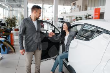 Man and woman buying new car in showroom. Male and female customers choosing vehicle in dealership, automobile sale, auto purchase