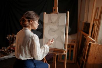 Female painter in studio, pencil sketch on easel. Creative paint, woman drawing portrait, workshop interior on background