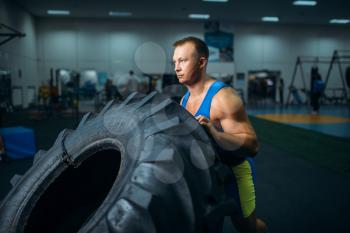 Strong male athlete doing strength exercise with truck tyre in gym, crossfit workout. Cross fit training in fitness club