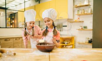 Two little girls cooks in caps adds butter to the bowl, cookies preparation on the kitchen. Kids cooking pastry, children chefs makes dough, child preparing cake