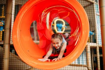 Funny girl climbing the maze in children game center. Excited child having fun on playground indoors. Female kid playing in amusement centre