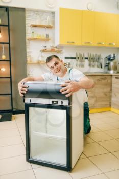 Worker in uniform hugs refrigerator at home. Repairing of fridge occupation, professional service
