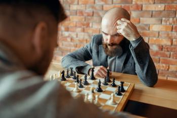 Male chess players playing, thinking process. Two chessplayers begin the intellectual tournament indoors. Chessboard on wooden table, strategy game