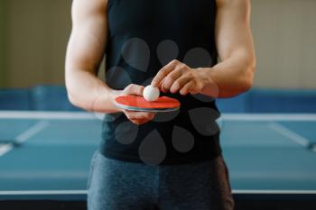 Male person holds racket and ping pong ball on it, workout indoors. Man in sportswear on training in table-tennis club