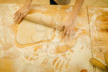 Little girl chef hands roll out the dough with rolling pin, cookies preparation on the kitchen, funny baker. Kids cooking pastry, child cook makes dough, children preparing cake