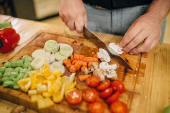 Chef hands with knife cuts mushrooms on wooden board closeup. Man cutting vegetables on counter, fresh salad cooking, kitchen interior on background. Male person chopping ingredients for lettuce