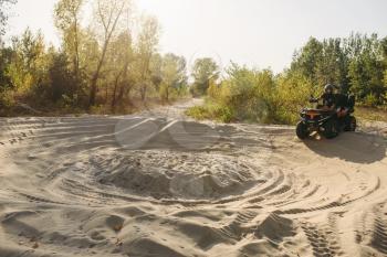 Atv rider in helmet climbing sandy road in forest, sunshine on background. Offroad riding on quad bike, extreme sport and travelling, quadbike adventure