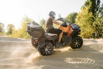 Atv riding in sand quarry, dust clouds. Male driver in helmet on quad bike, extreme freeriding on quadbike in desert dunes