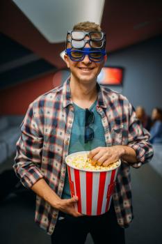 Male spectator in 3d glasses holds popcorn in cinema hall before the showtime. Man in movie theater, entertainment lifestyle
