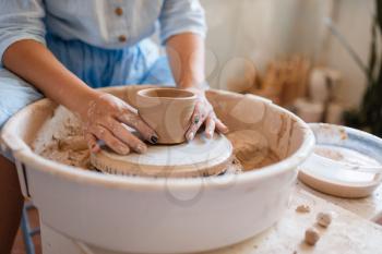 Female master holds wet pot over the pottery wheel. Woman molding a bowl. Handmade ceramic art, tableware from clay