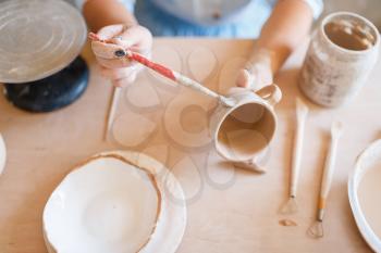 Female potter paints a pot, pottery workshop. Woman molding a bowl. Handmade ceramic art, tableware from clay