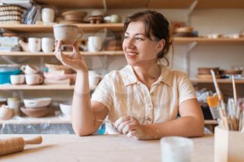 Female master holds fresh painted pot, pottery workshop. Woman molding a bowl. Handmade ceramic art, tableware from clay
