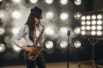 Female jazz musician in hat plays the saxophone on the stage with spotlights. Jazz performer playing on the scene