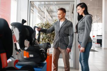 Couple buying child car seat in showroom. Male and female customers looks vehicle in dealership, automobile sale, auto purchase