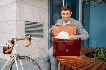 Businessman bicyclist in suit puts document into the briefcase in downtown. Business person riding on eco transport on city street