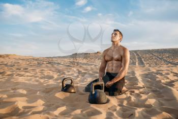 Male athlete sitting on sand after workout in desert at sunny day. Strong motivation in sport, strength outdoor training