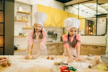 Two little girls chefs crumple the dough, cookies preparation on the kitchen, funny bakers. Kids cooking pastry, children cooks preparing cake