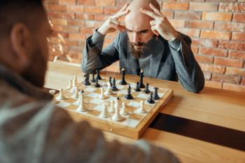 Male chess players playing, thinking process. Two chessplayers begin the intellectual tournament indoors. Chessboard on wooden table, strategy game