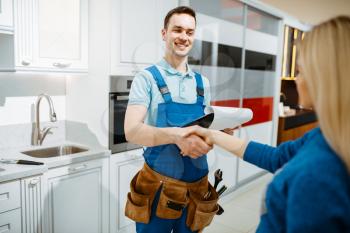 Male plumber in uniform and female customer in the kitchen. Handyman with toolbag repair sink, sanitary equipment service at home