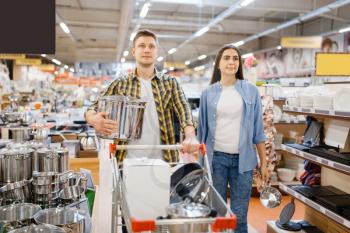 Young couple with cart in houseware store. Man and woman buying home goods in market, family in kitchenware supply shop