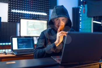Hacker in hood shows thumbs up at his workplace with laptop and PC, password or account hacking. Internet spy, crime lifestyle