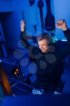 Male gamer with raised hands, tournament winner, gaming lifestyle, cybersport. Computer games streaming, videogame player in his room with neon light