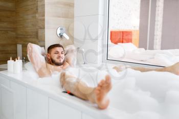 Man lying in bath with foam in the morning. Male person relax in bathroom, skin and body treatments procedures