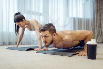 Morning fitness training of family couple at home. Active man and woman in sportswear doing push up exercise in their house, healthy lifestyle, physical culture