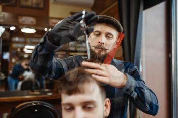 Barber with comb and scissors makes stylish haircut to a client. Professional barbershop is a trendy occupation. Male hairdresser and customer in retro style hair salon
