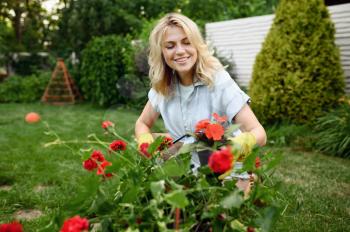 Happy young woman in gloves works with flower in the garden. Female gardener takes care of plants outdoor, gardening hobby, florist lifestyle and leisure