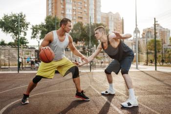 Two players in the center of the basketball field on outdoor court. Male athletes in sportswear play the game on streetball training