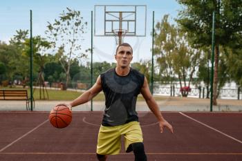Basketball player with ball in motion on outdoor court. Male athlete in sportswear shoots on streetball training, jump in action