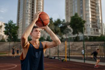Basketball player makes a throw on outdoor court. Male athlete in sportswear shoots on streetball training, jump in action