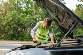 Young man in the reflective vest at the opened hood, car breakdown. Broken automobile or repairing of vehicle, trouble with auto engine on highway