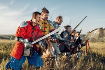 Medieval knights in armor and helmets standing in a row before battle. Armored ancient warrior in armour posing in the field