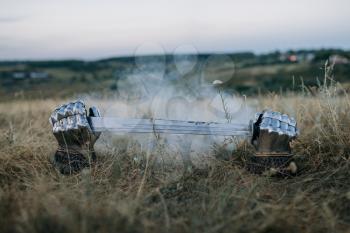 Metal gloves and sword sticking out of the ground, nobody, great warriors symbol in the middle of the field