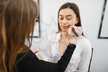 Cosmetologist applies makeup on a woman's face in cosmetics store. Luxury beauty shop salon, female customer and beautician in fashion market