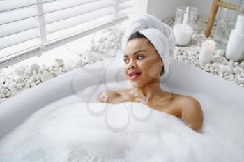 Seductive woman relax in a bubble bath. Female person in bathtub, beauty and health care in spa, wellness treathment in bathroom, pebbles and candles on background