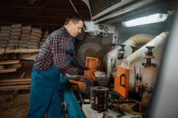 Carpenter in uniform near woodworking machine, lumber industry, carpentry. Wood processing on factory, forest sawing in lumberyard