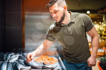 Man choosing fresh chilled fish in grocery store. Male person buying frozen food in market, customer shopping products in supermarket