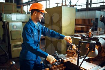 Worker in uniform and helmet works on lathe, factory. Industrial production, metalwork engineering, power machines manufacturing