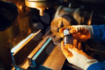Male worker hands holds detail, lathe on background, plant. Industrial production, metalwork engineering, power machines manufacturing